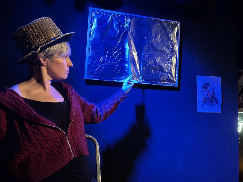 Cassie (Laura Shipler Chico) in a sparkly hat anxiously peers at a sealed-up window