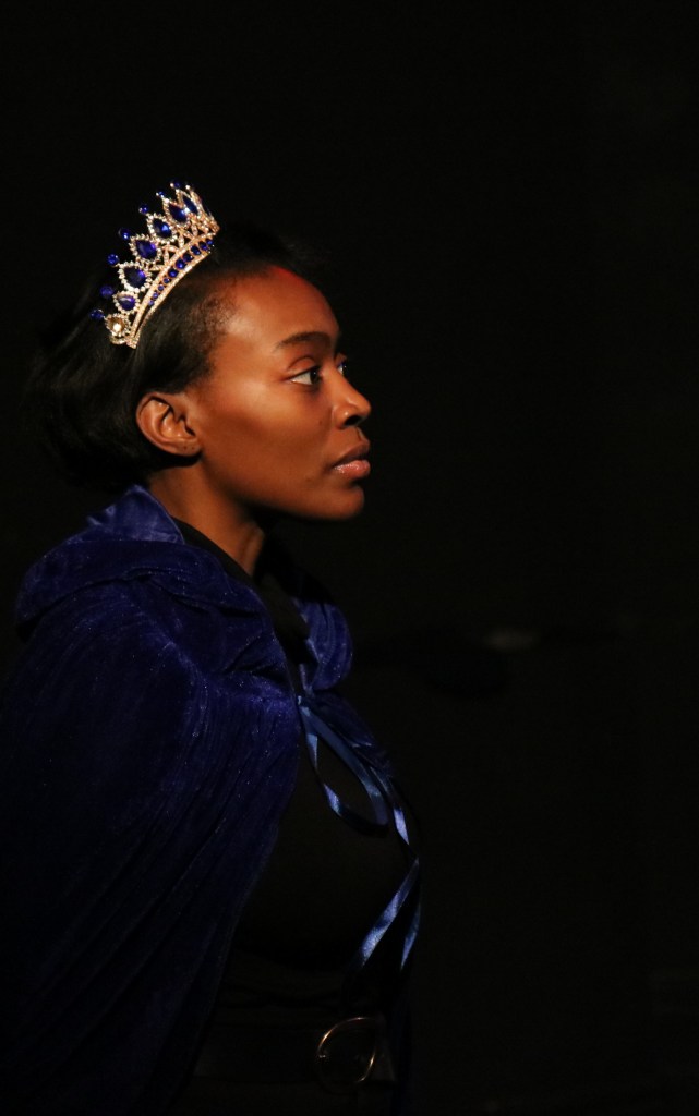 Hannah Omisore (the Princess) wearing a tiara and blue velvet cape gazing to the right