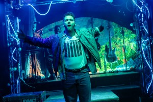 Simon Parkes (played by Max Runham) arms spread, wearing a bomber jacket, T-shirt and jeans, looking defiantly towards the viewer.