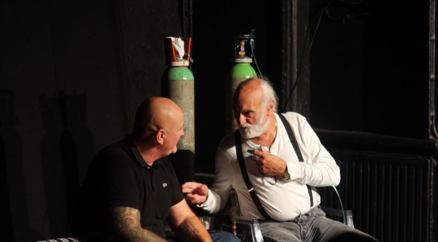 Sitting on the left in a black Lacoste polo shirt Danny Boy (played by Francis Saunders); sitting on the right in white vest top and black braces Arthur (played by Sidney Kean) with two large oxygen tanks behind him.