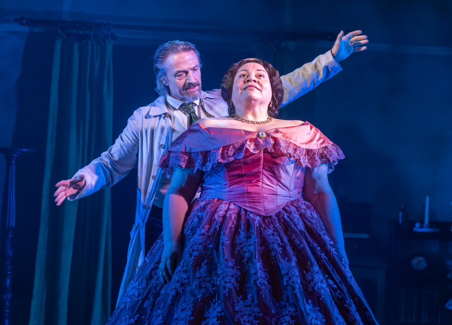 Matthew Brady (Hal Fowler) arms spread wide behind Mary Lincoln (Keala Settle) standing bathed in light in an elaborate pink Victorian dress.