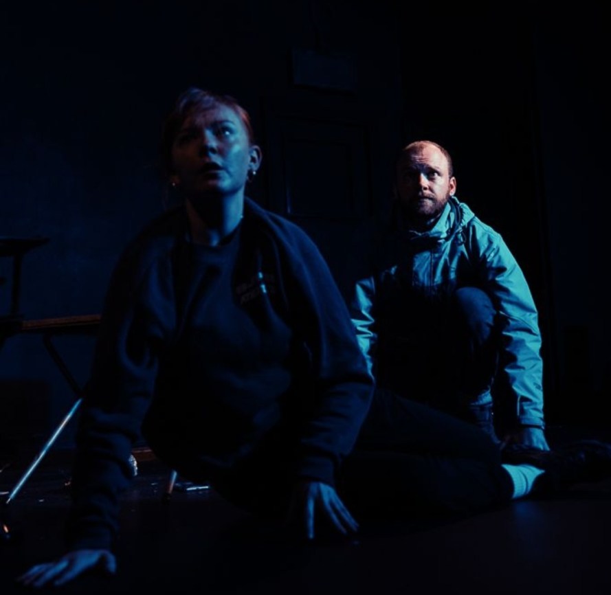 Night scene, dimly lit. In front on the left is Ffion (played by Lucy Havard) looking up; on the right at the back is Ben (played by Andy Sellers) in a light blue cagoule, also looking up.