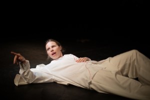 Yanina Hope lying on the ground in white shirt and trousers and pointing